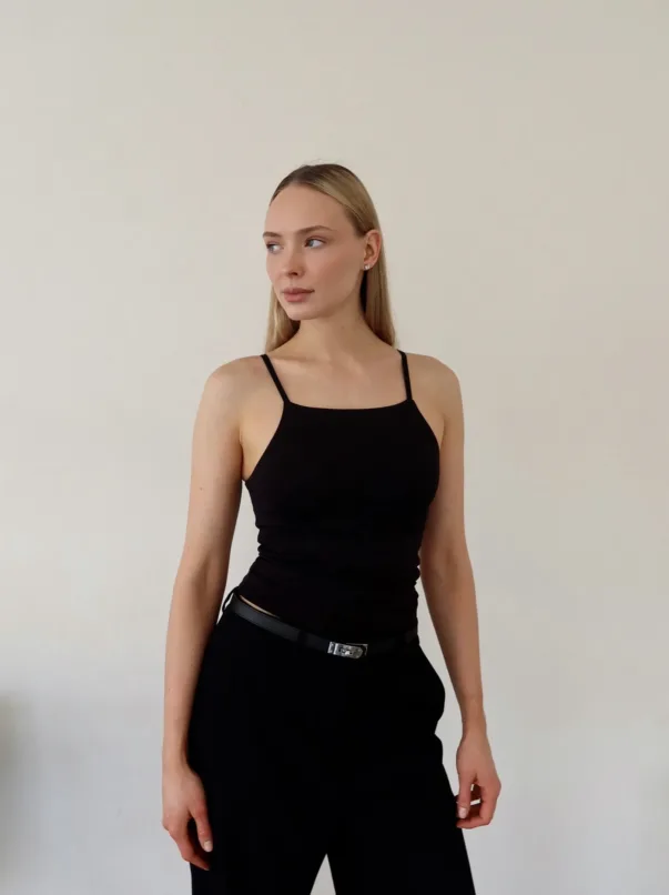 Edited in Tezza with Contrast Exposure HSL Grain Temperature Woman in a black sleeveless dress with spaghetti straps, standing against a plain light wall, looking to her left.