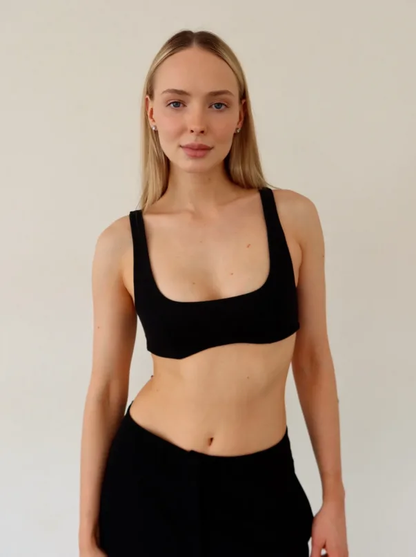 Front view of a young woman with blonde hair wearing a black sports bra against a light wall.