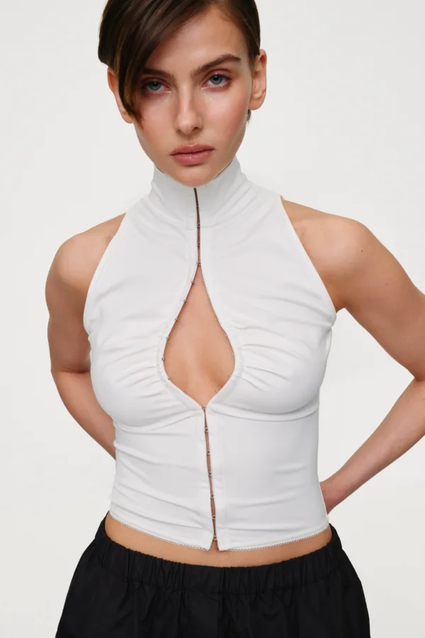 Model wearing a white sleeveless zip-front top with decorative seams, standing against a plain light background.