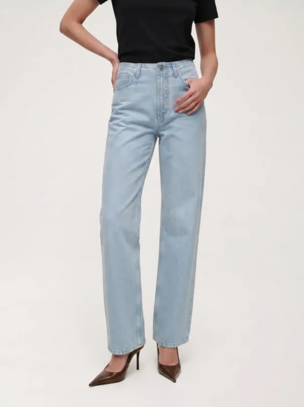 Full-length shot of a person wearing light-wash high-waisted jeans, a black top, and brown pointed-toe heels, with hands on hips.