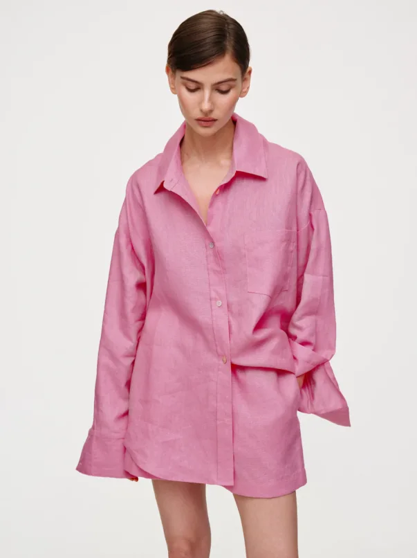 Person in a loose pink button-down shirt looking down, against a white background.