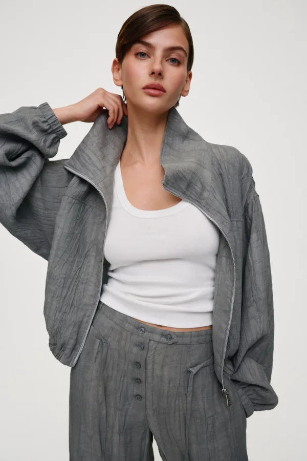Woman model wearing a gray textured suit jacket and matching high-waisted pants with a white top, posing with hand near her neck.