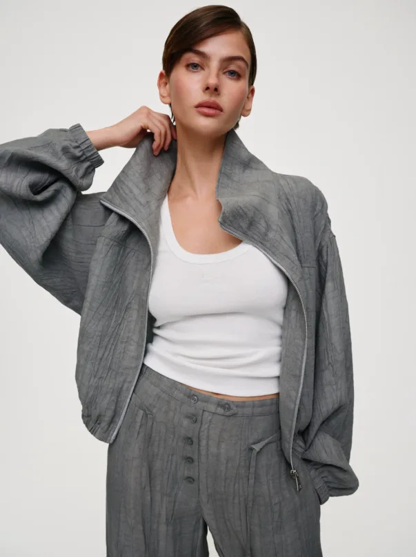Woman model wearing a gray textured suit jacket and matching high-waisted pants with a white top, posing with hand near her neck.