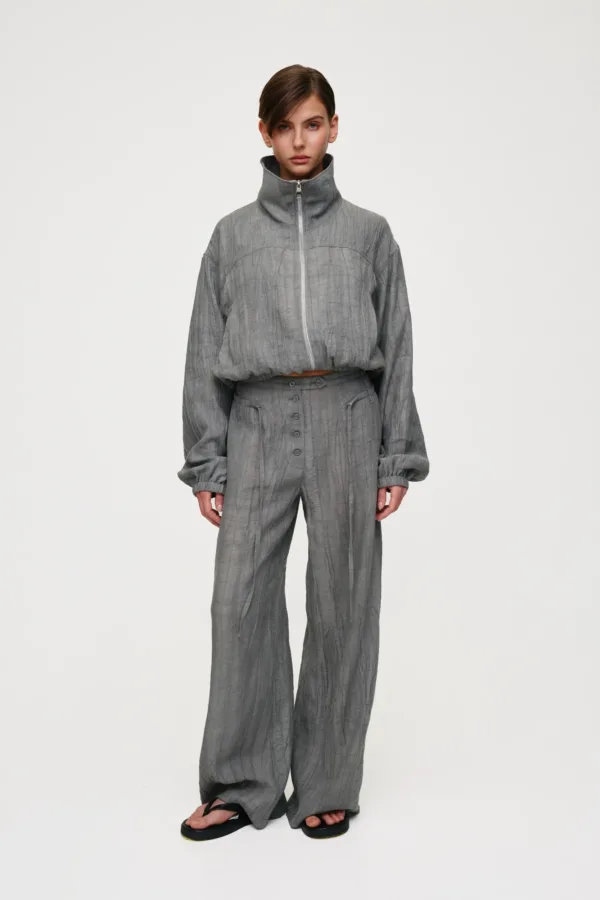 Model wearing a gray crinkled zip-front high-neck top with matching wide-leg pants, standing against a pale background.