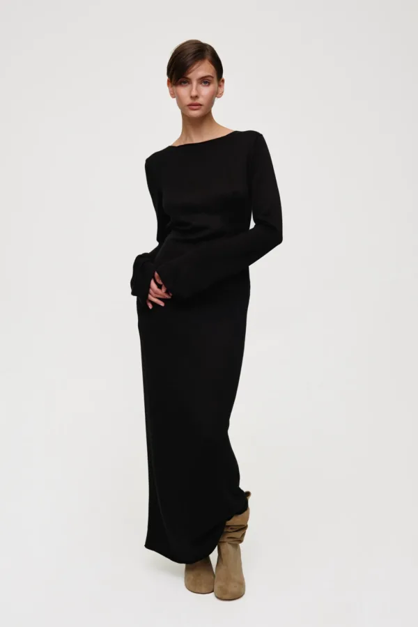 Model wearing a black long-sleeve knit dress with tan knee‑high suede boots, standing against a light background.