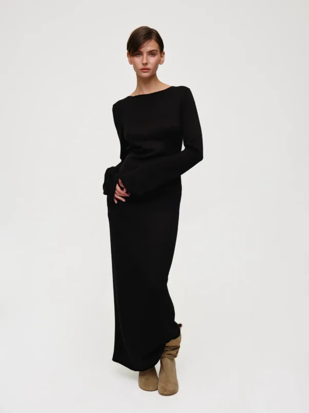 Model wearing a black long-sleeve knit dress with tan knee‑high suede boots, standing against a light background.
