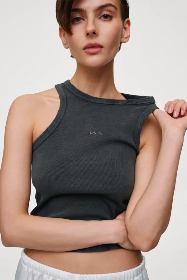 Person standing with arms crossed, wearing a dark gray ribbed sleeveless top against a neutral background.