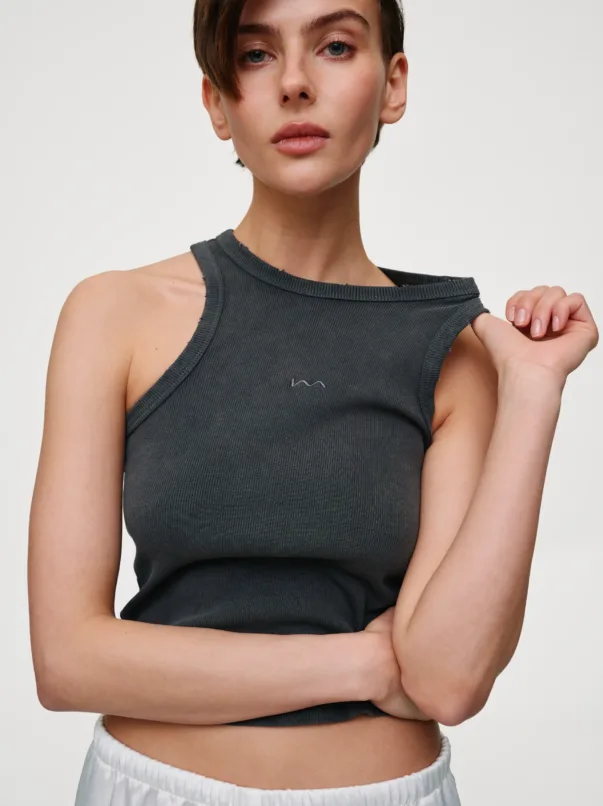 Person standing with arms crossed, wearing a dark gray ribbed sleeveless top against a neutral background.