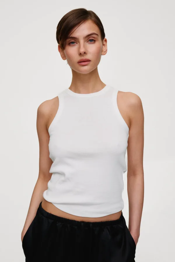 Portrait of a woman wearing a white sleeveless tank top against a light background.