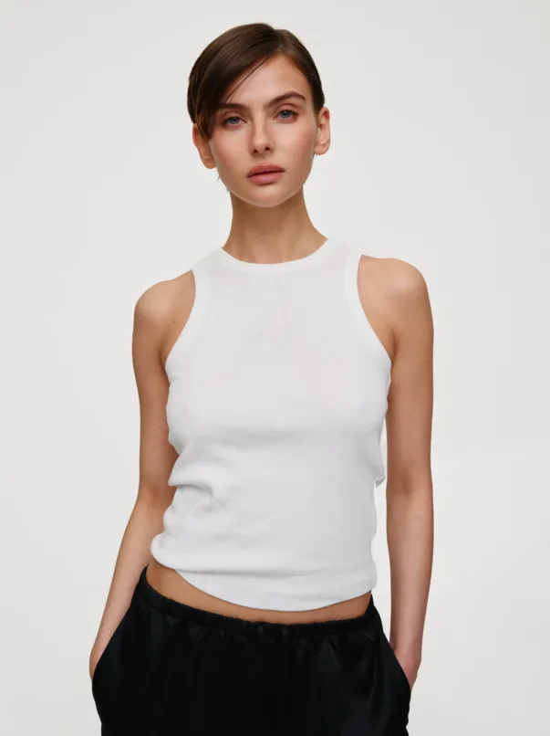 Portrait of a woman wearing a white sleeveless tank top against a light background.
