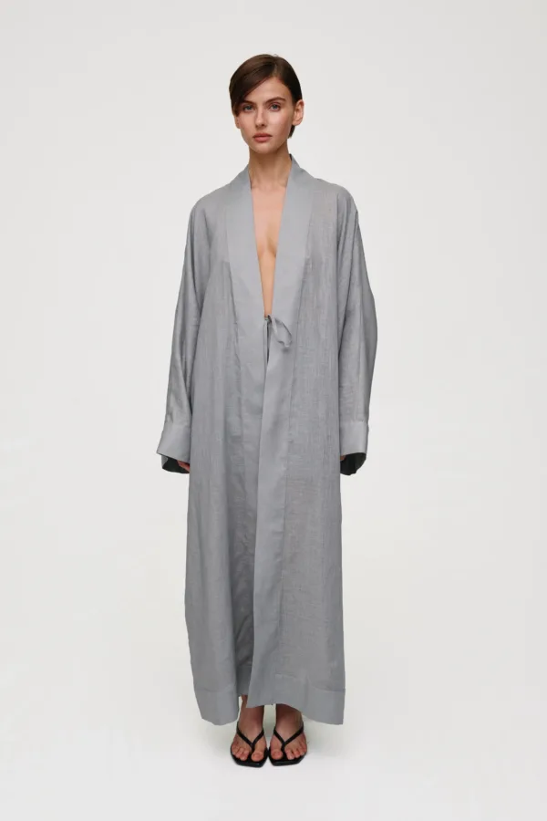 Model wearing a loose gray robe with a waist tie, standing against a pale background, wearing black strappy sandals.