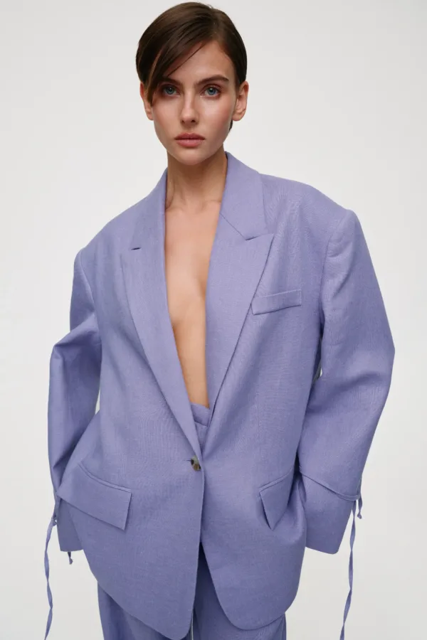 Woman posing in a lavender blazer with wide lapels, open at the chest, against a neutral light background.