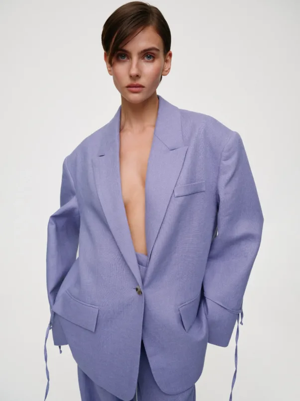 Woman posing in a lavender blazer with wide lapels, open at the chest, against a neutral light background.