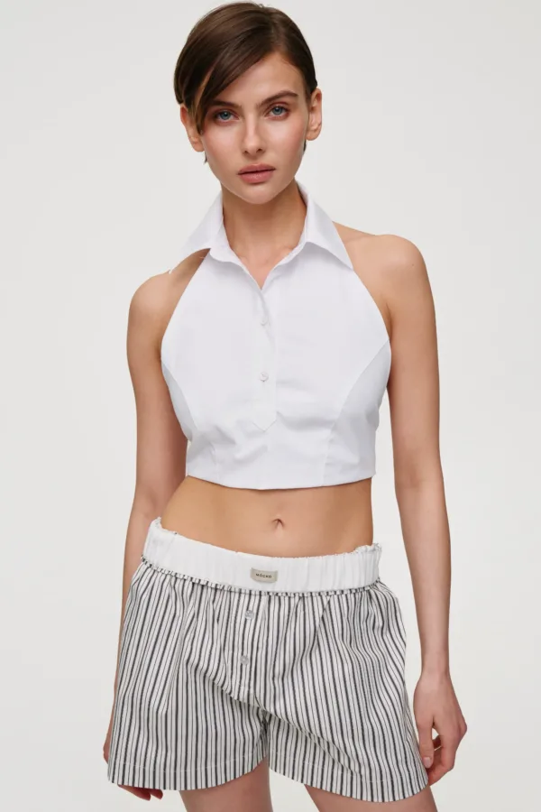 Female model wearing a white cropped button-down top with a structured collar and high-waisted striped shorts, standing against a light background.