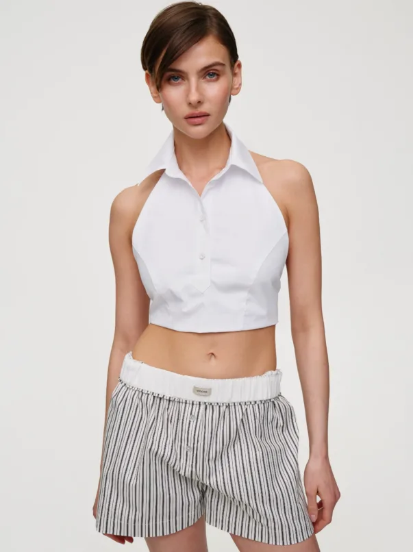 Female model wearing a white cropped button-down top with a structured collar and high-waisted striped shorts, standing against a light background.