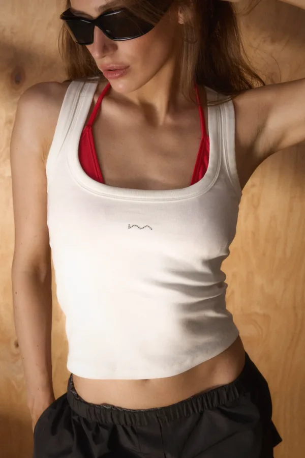 Woman wearing a white tank top over a red bikini top, with black sunglasses, standing against a wooden background.